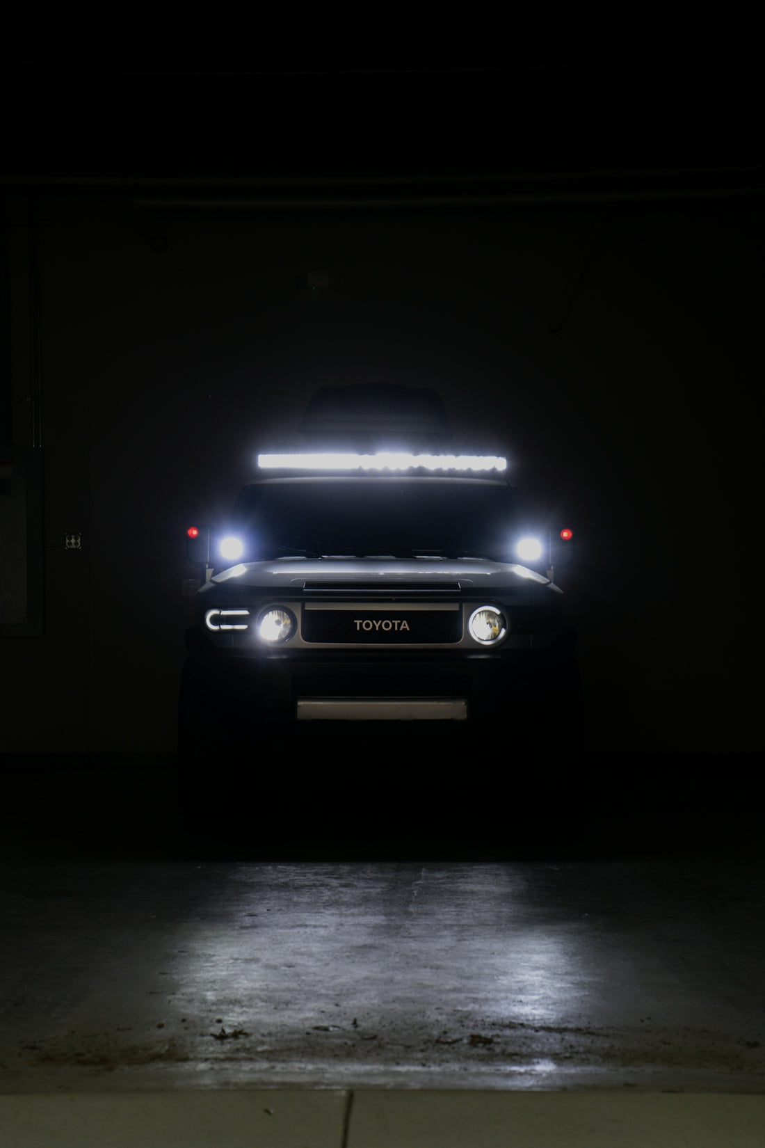 A dark toyota fj cruiser with bright lights in darkness.