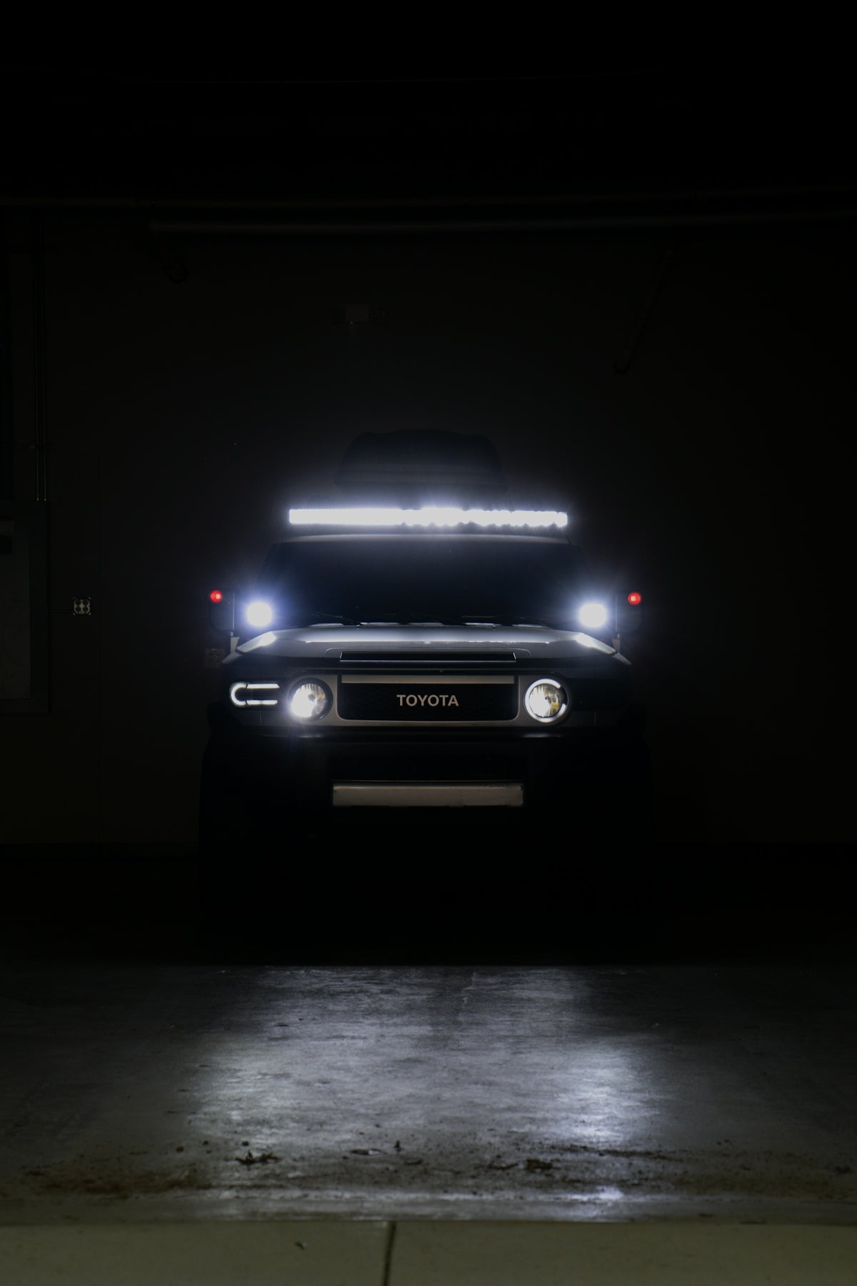A dark toyota fj cruiser with bright lights in darkness.