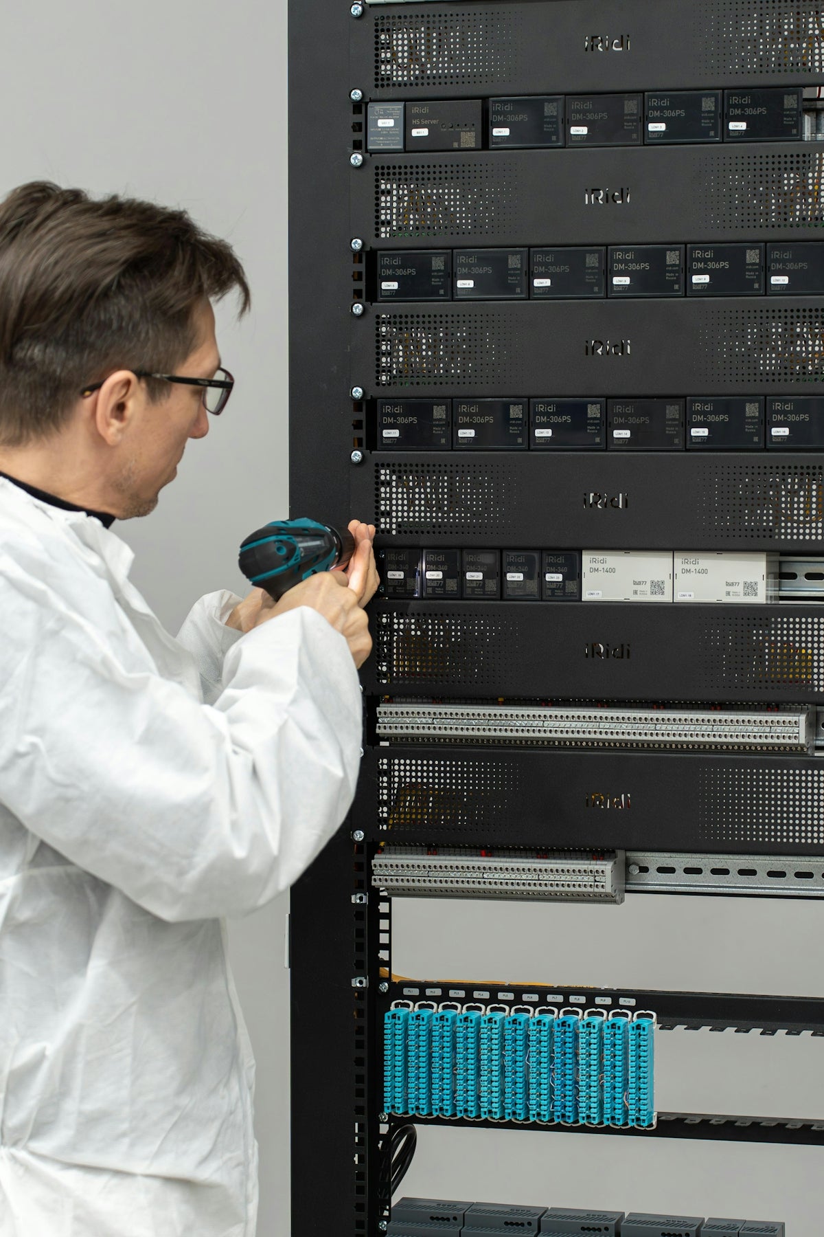 Man in lab coat installing server equipment with power tool